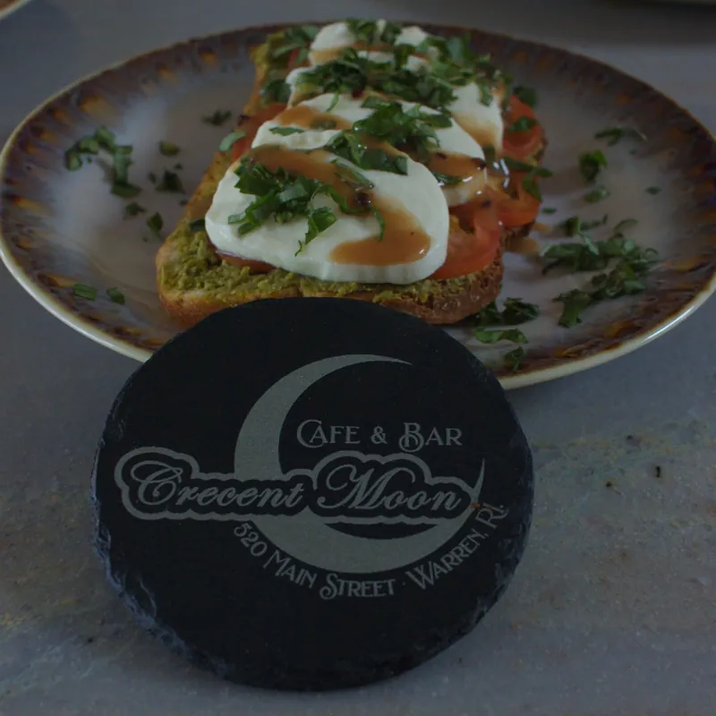 Caprese toast with fresh mozzarella, tomato, basil, and balsamic beside a branded Crescent Moon slate coaster