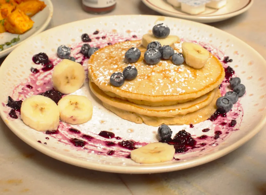 Buttermilk pancakes with fresh blueberries, banana slices, powdered sugar, and blueberry compote