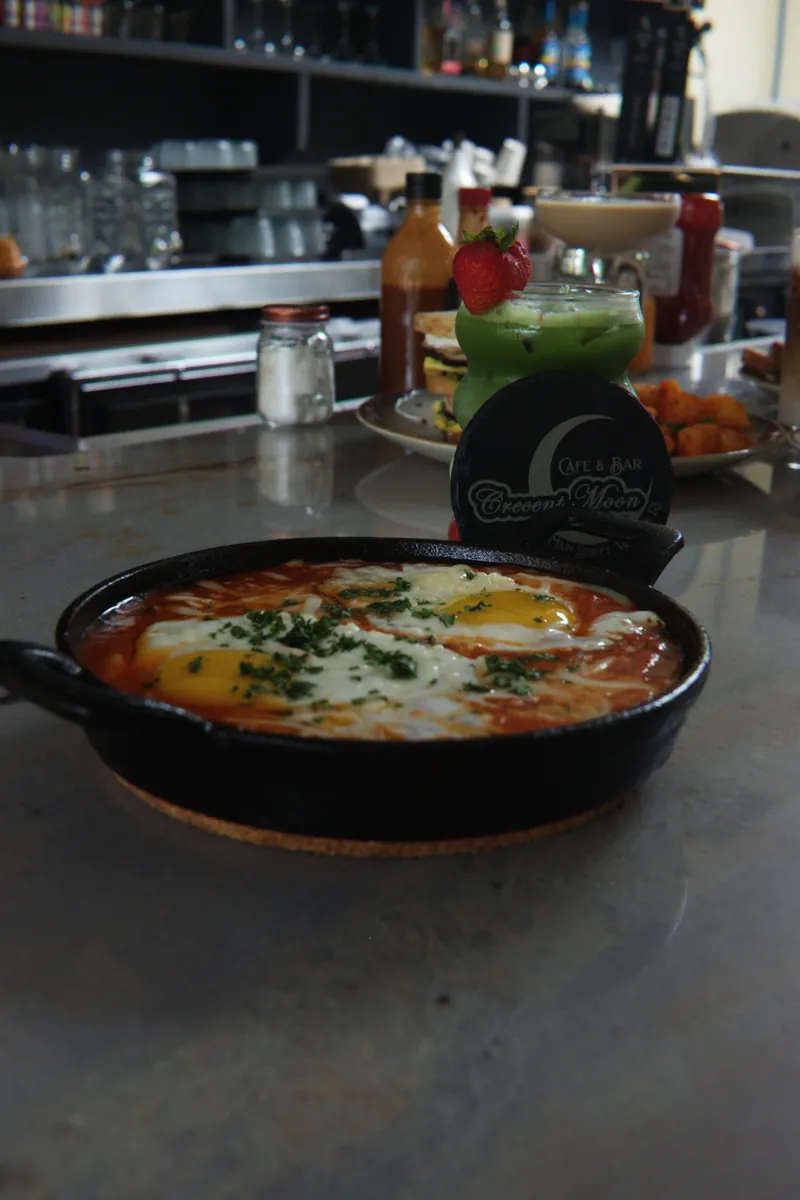 Shakshuka baked eggs in a cast iron skillet at the bar with a branded Crescent Moon coaster